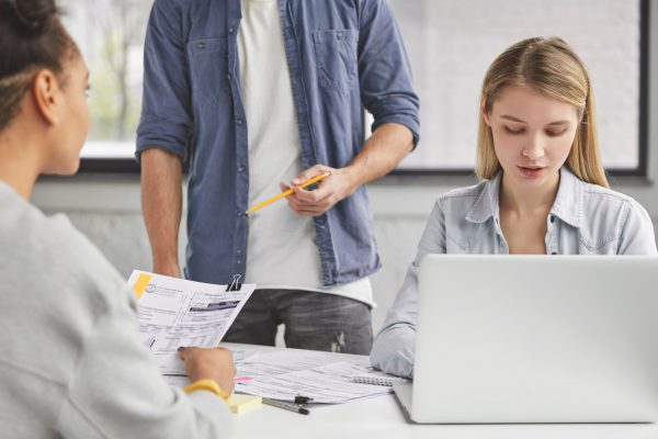 Cropped image of female copywriter works on laptop computer and her colleagues look attentively at d